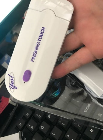 Hand holding a white electronic device labeled 'Finishing Touch' on a blurred background