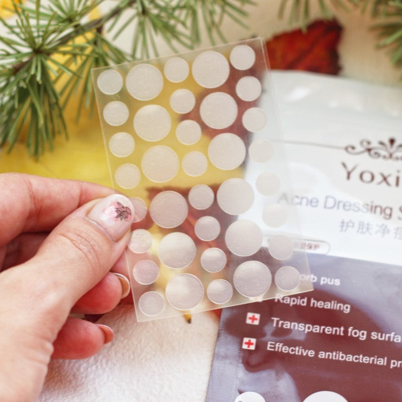 Hand holding a sheet of round white stickers with a product packaging in the background.