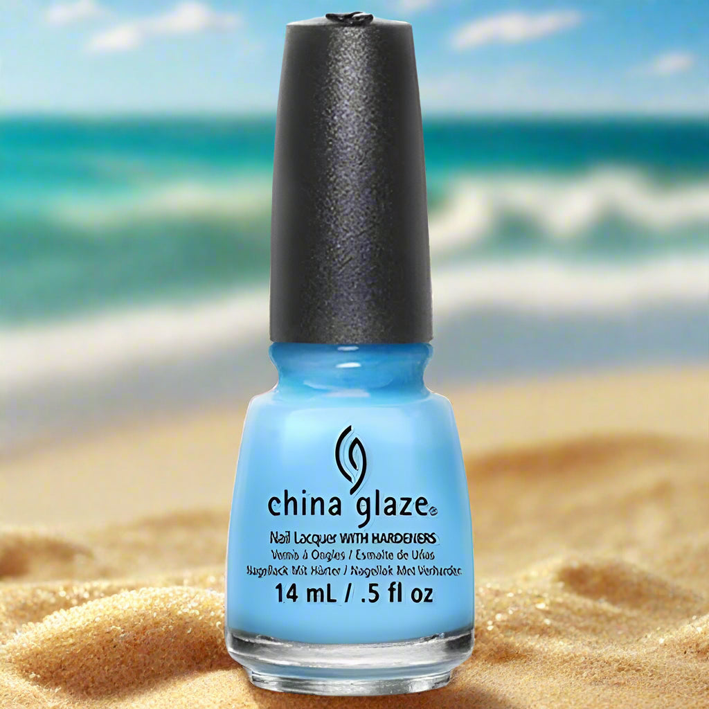 Blue nail polish bottle with black cap on sand and ocean background