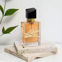 Perfume bottle with a black cap on a white surface with a plant in the background