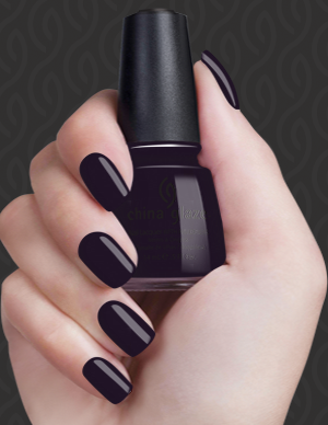 Hand with dark nail polish holding a black nail polish bottle against a dark background