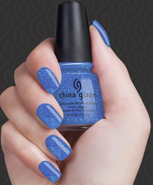 Hand with blue glittery nail polish holding a bottle of China Glaze nail polish.